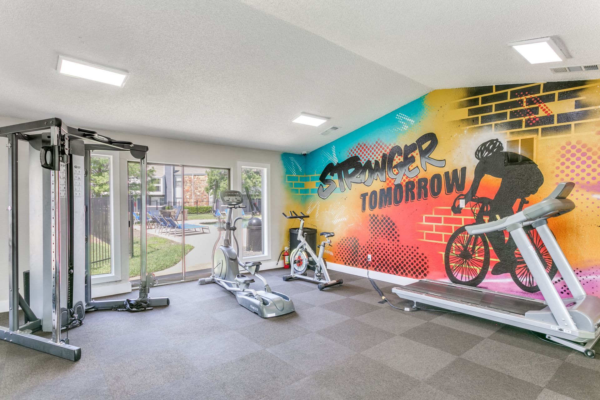 Gym with exercise equipment, including a treadmill and weight machine, with a colorful mural on the wall.