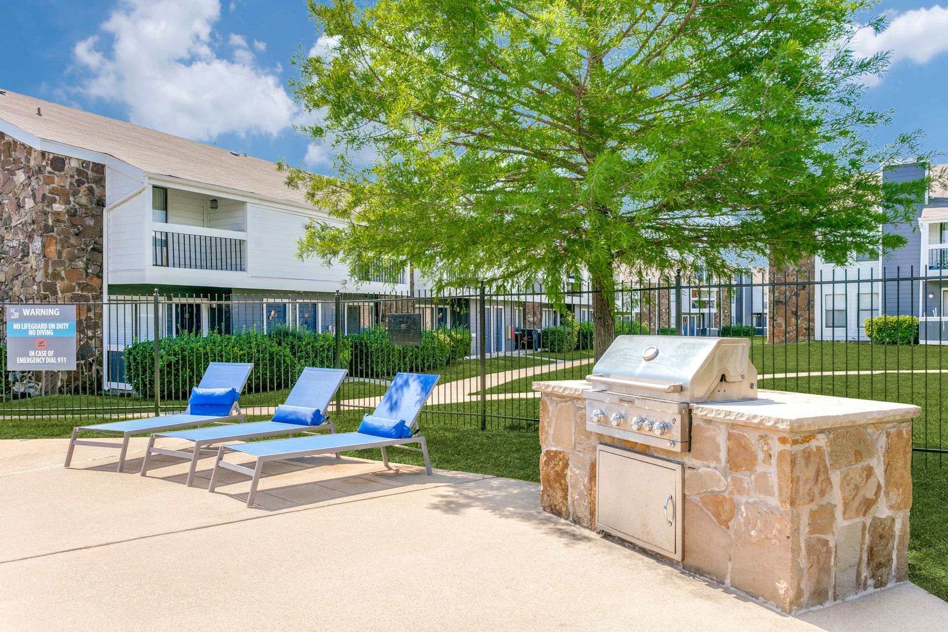 Outdoor grilling area with stone facade, lounge chairs, and apartment buildings.