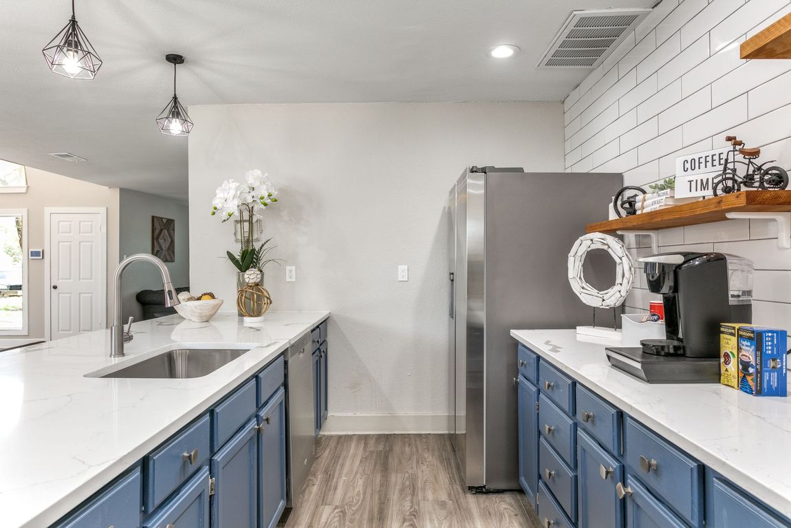 Modern kitchen with blue cabinets, white countertops, stainless steel appliances, and white brick accent wall.