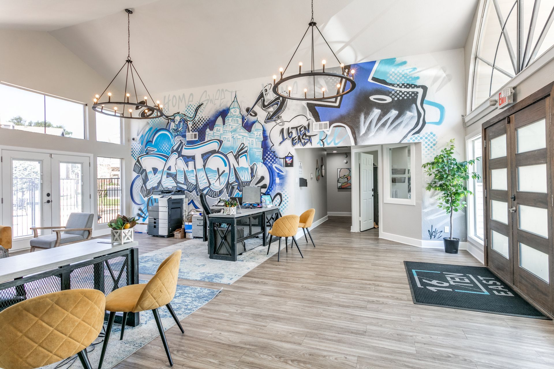 Lobby with a large blue mural, seating, desk, and chandelier lighting. Entrance door on the right.