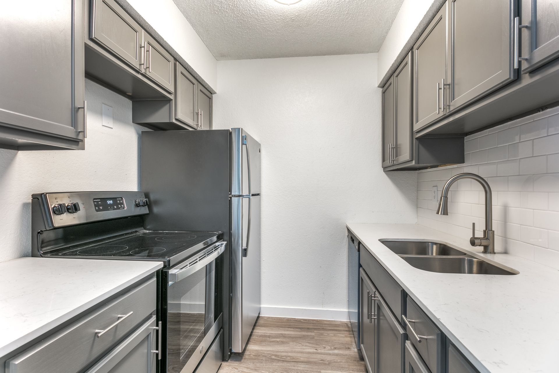Gray kitchen with upper and lower cabinets, stainless steel appliances, and white countertops.
