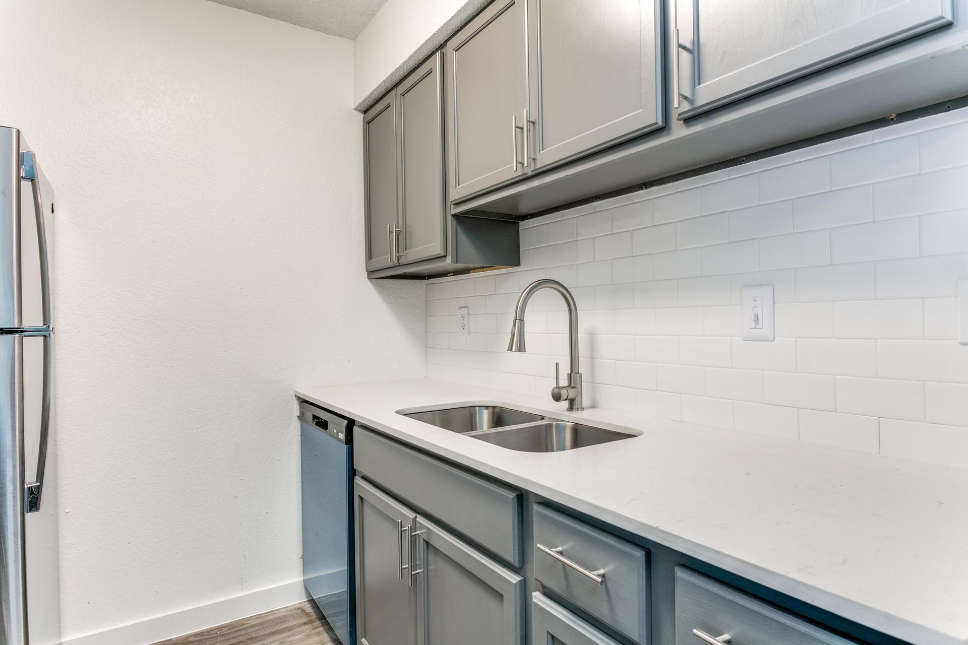 Modern kitchen with gray cabinets, white countertop, stainless steel sink, and white subway tile backsplash.