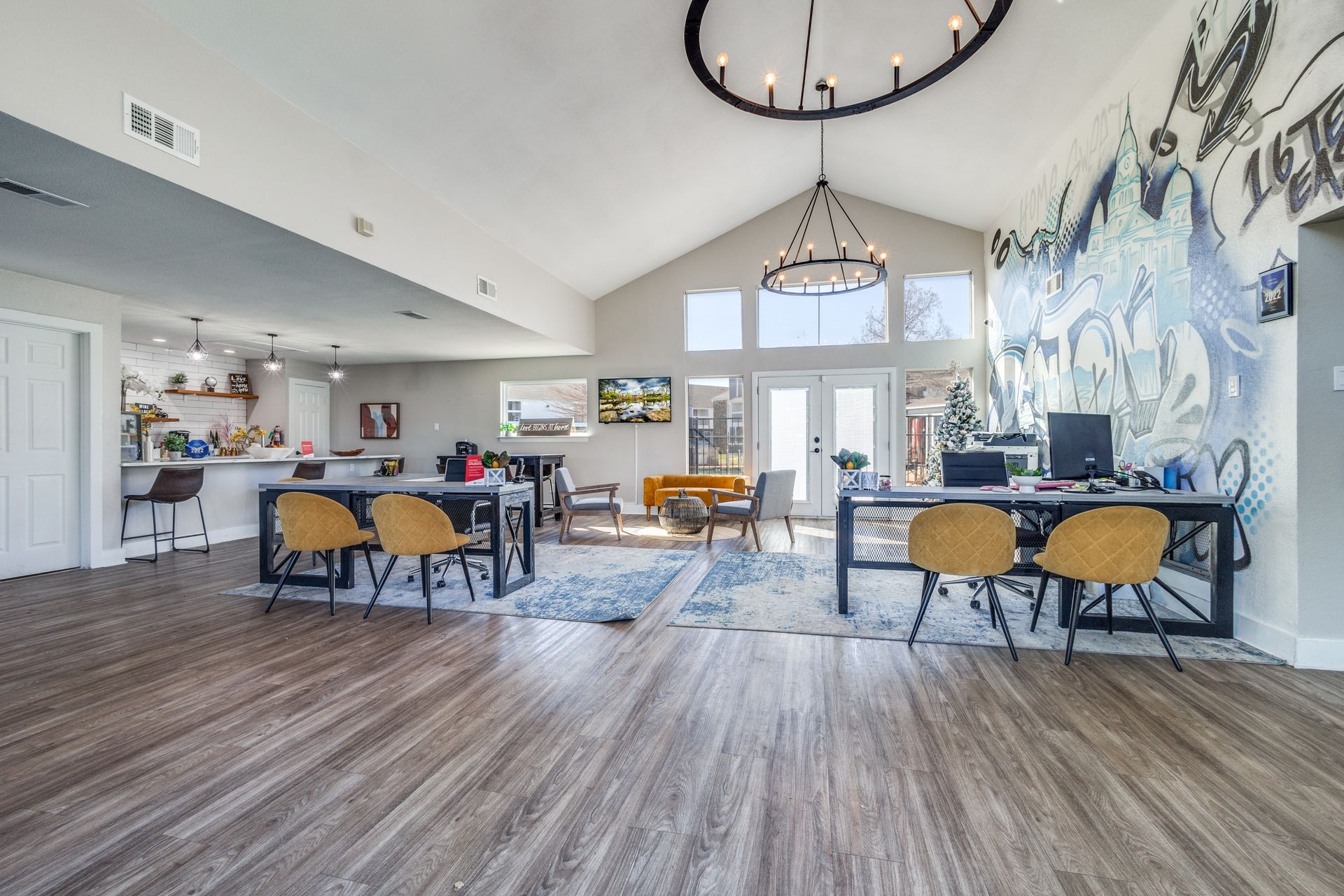 Spacious lobby with wood floors, two desks, yellow chairs, a bar, and a large mural.