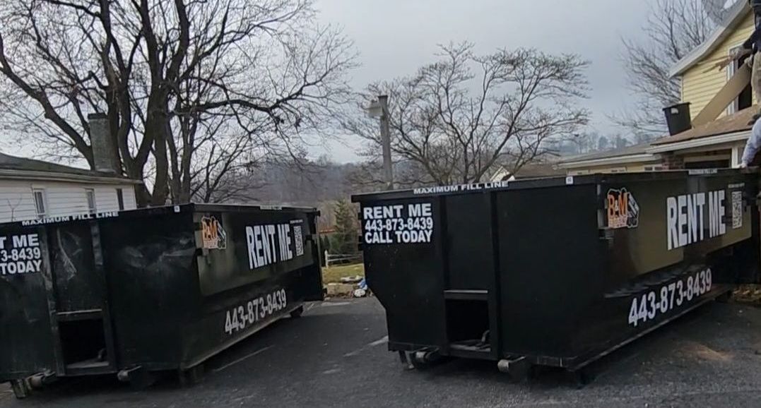 a large orange dumpster is parked next to a black dumpster that says rent