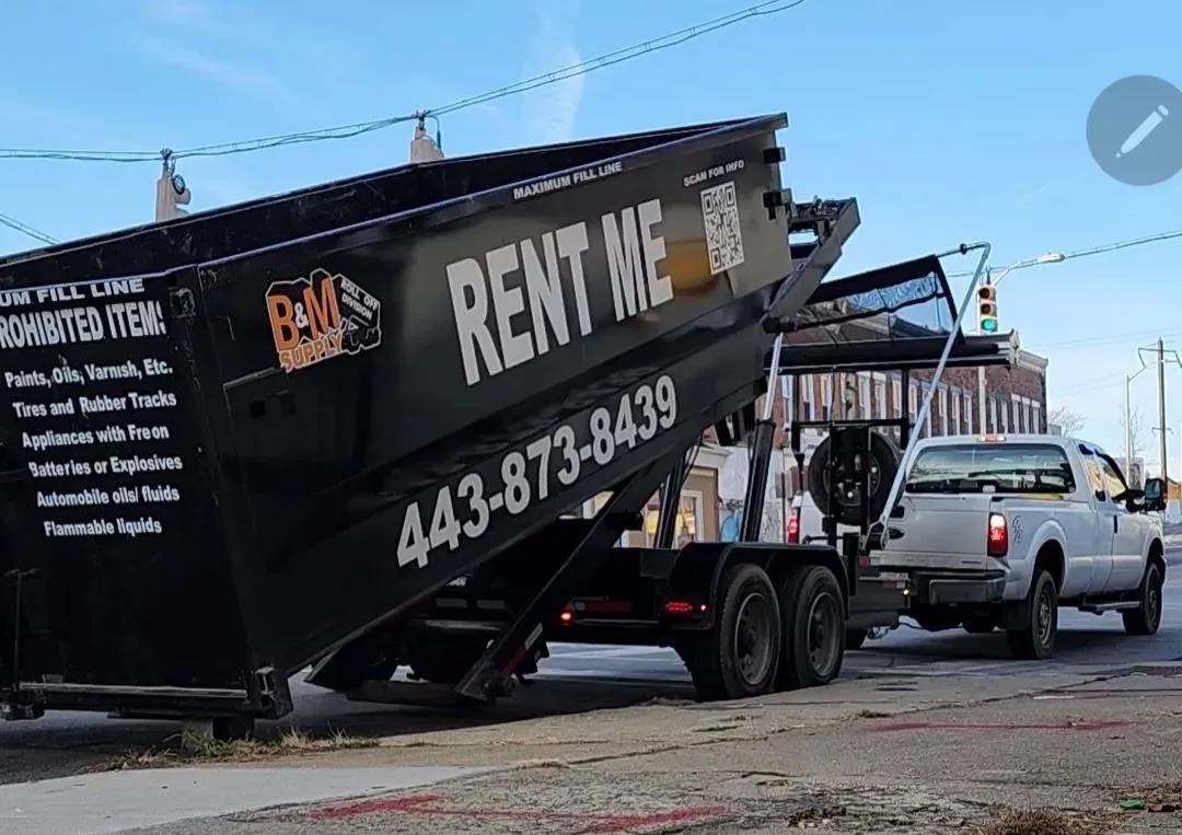 a large orange dumpster is parked next to a black dumpster that says rent