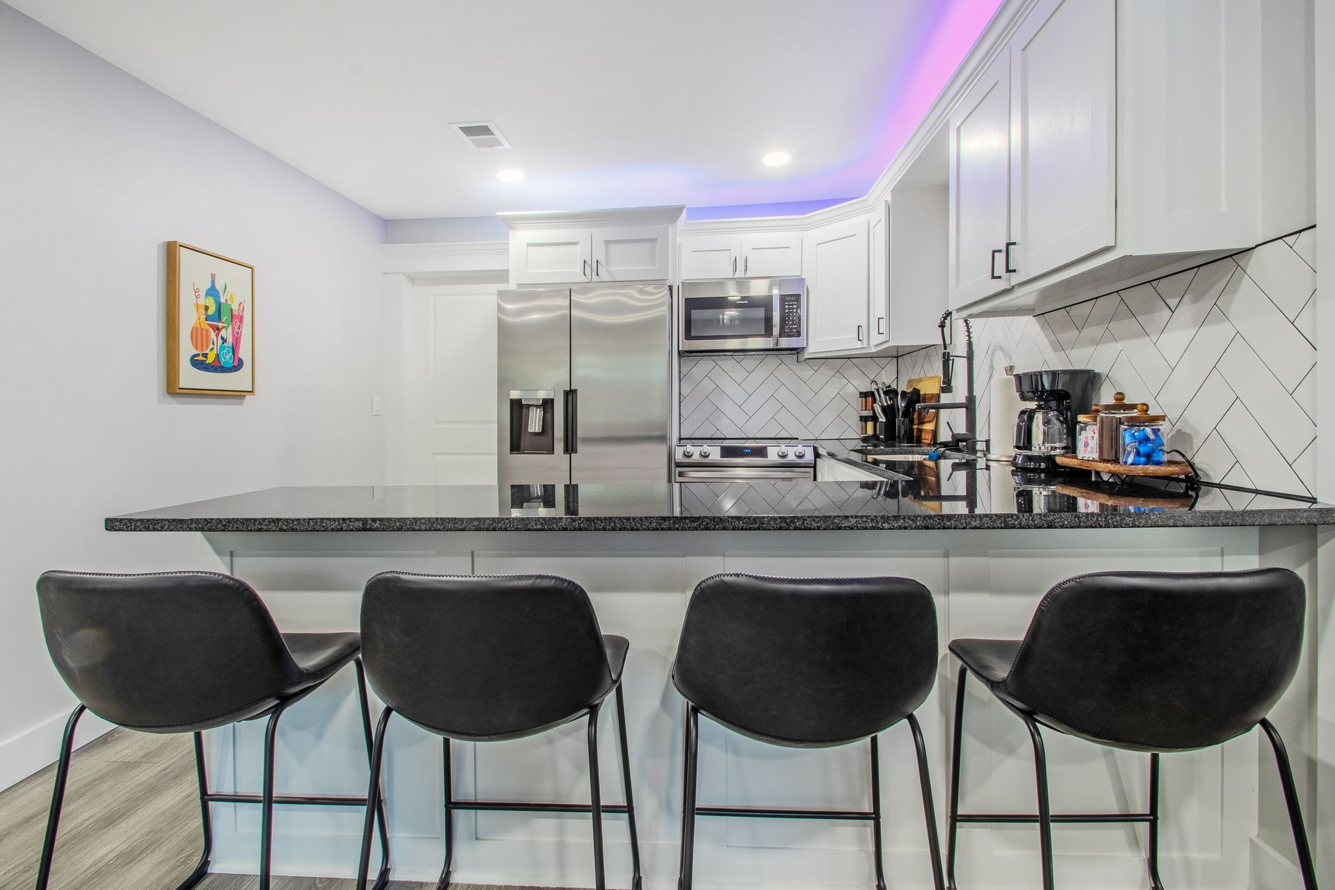A kitchen with stools and a purple light on the ceiling.