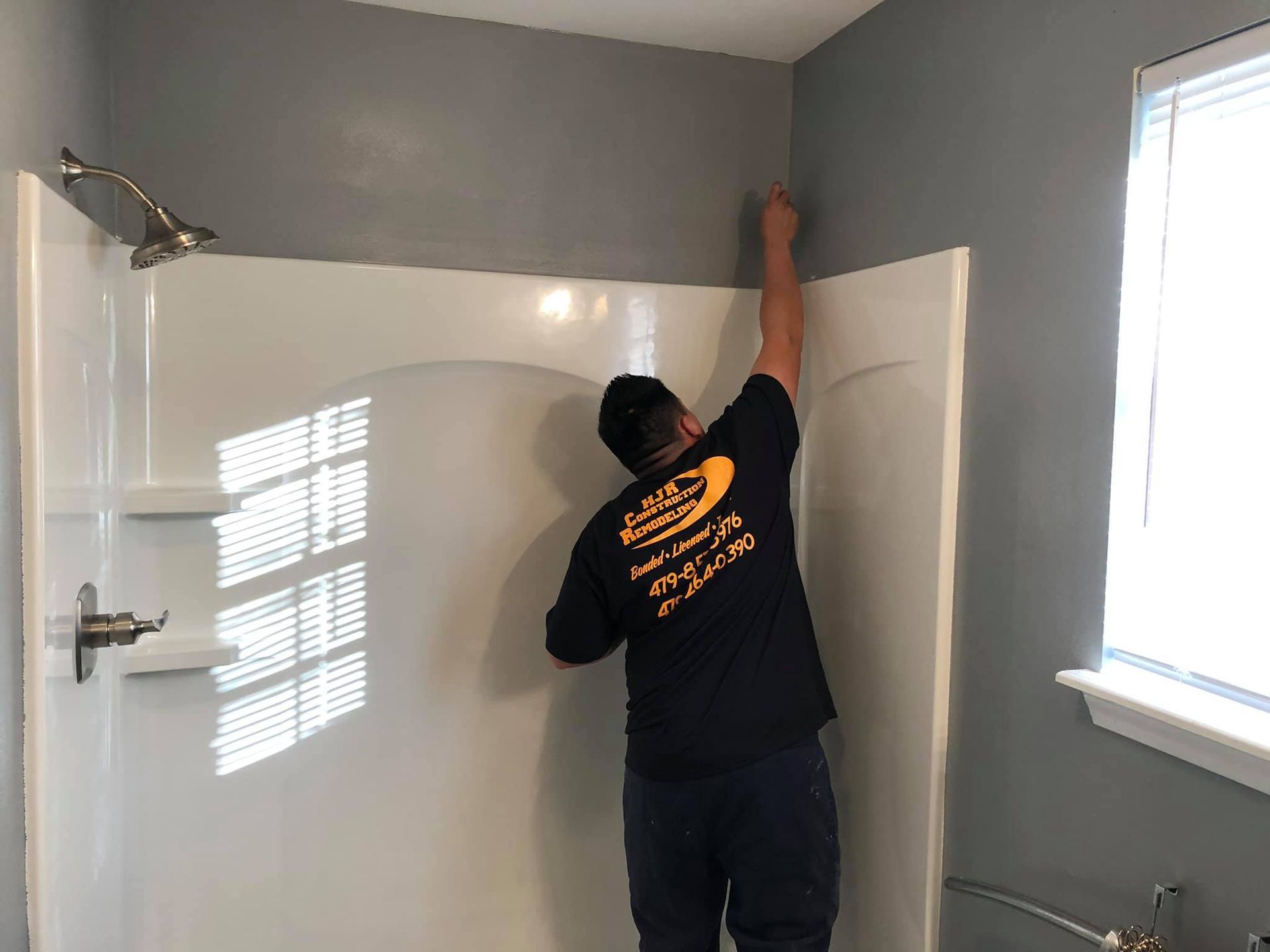 A man is installing a shower stall in a bathroom.