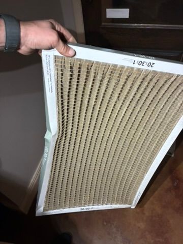 Hand holding a severely warped air filter; cardboard frame, beige filter media.