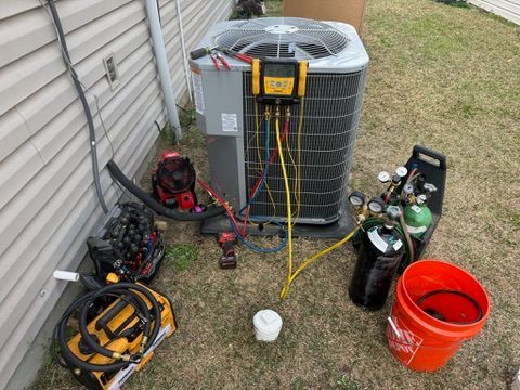 HVAC technician servicing an air conditioning unit. Equipment and tools are scattered on grass.
