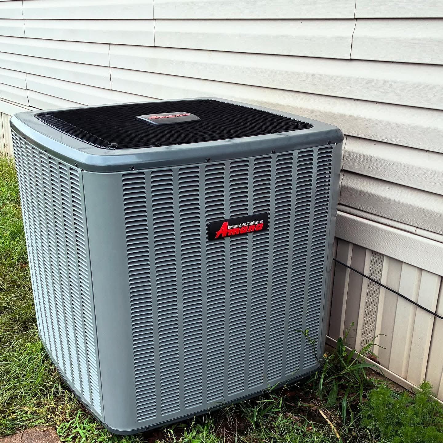 Gray air conditioning unit next to a white house with grass.