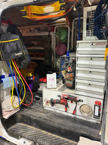 Inside of a service van, tools and equipment are stored on shelves and in drawers, with various hoses and a grinder visible.