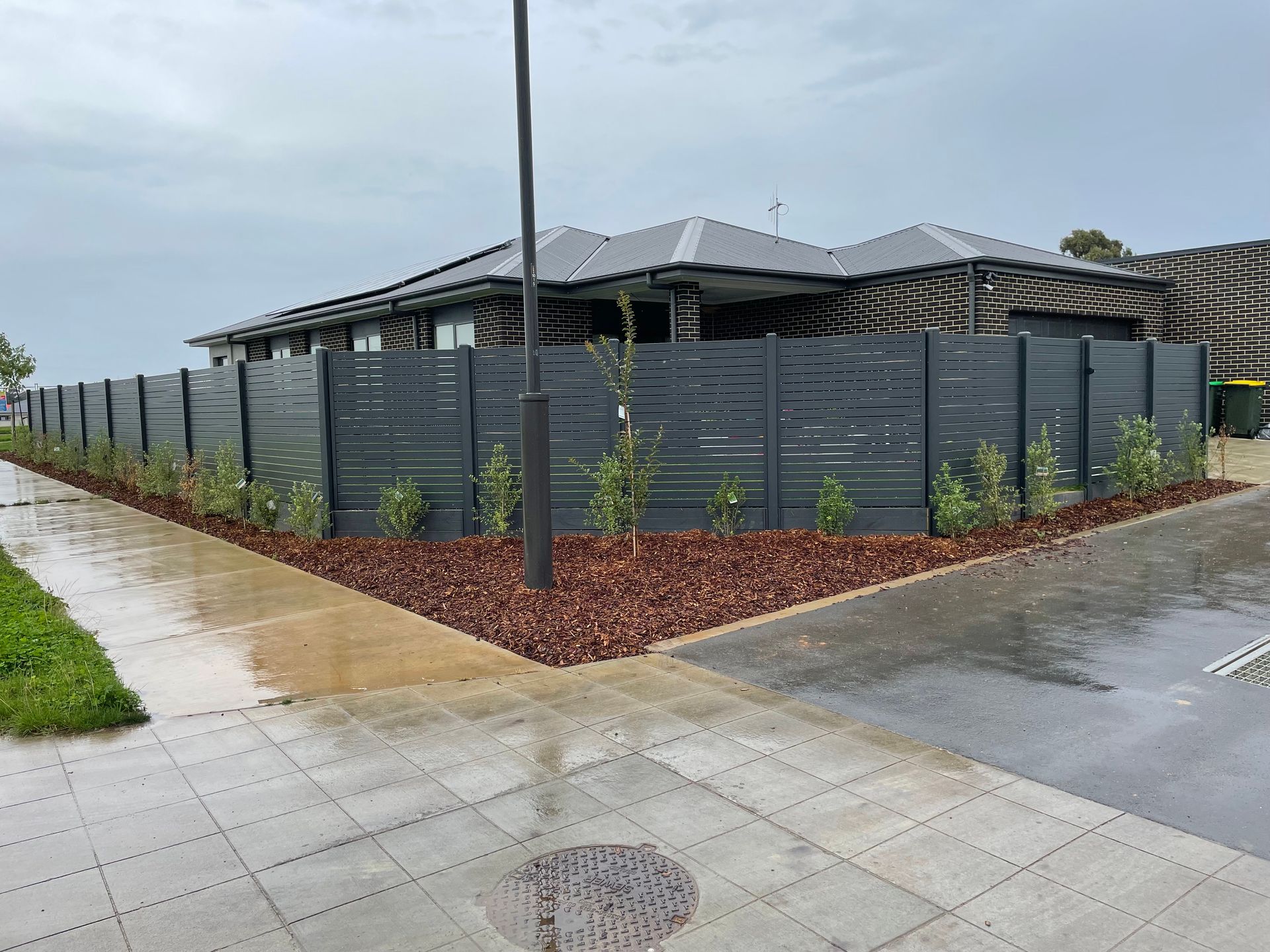 Gray Slat Fence Bordering a House on a Rainy Day — Capital Fencing in Charnwood, ACT