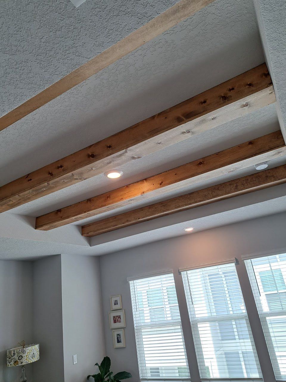 Wooden beams accent a gray ceiling with recessed lighting. Windows and light gray walls are below.