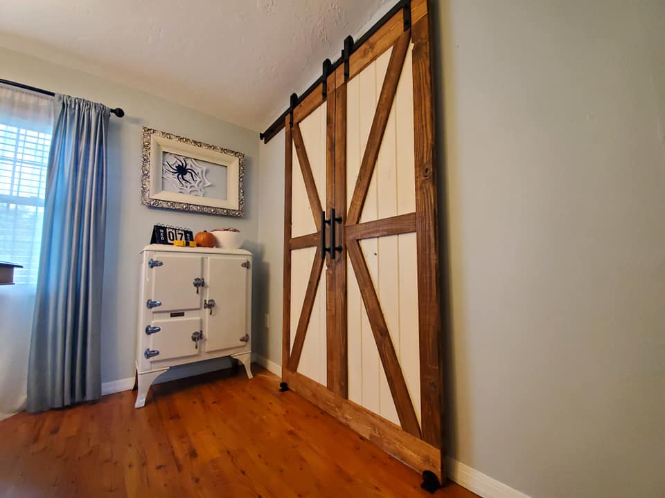 Barn-style sliding doors with white and wood panels, a white cabinet, and blue curtains in a room.