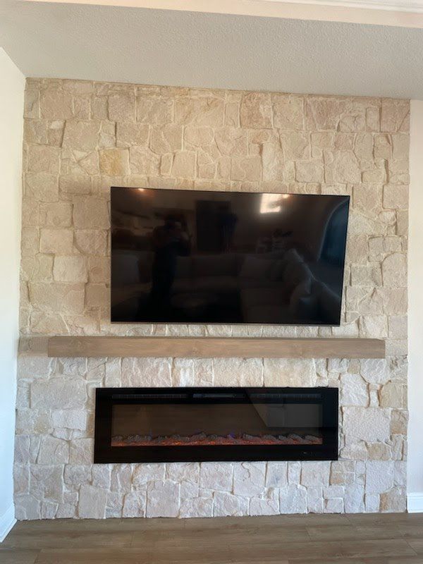 A modern fireplace with a mounted TV above it, set against a stone wall.