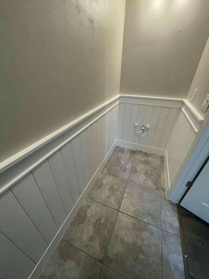 Bathroom with white wainscoting, gray tile floor, and a door.