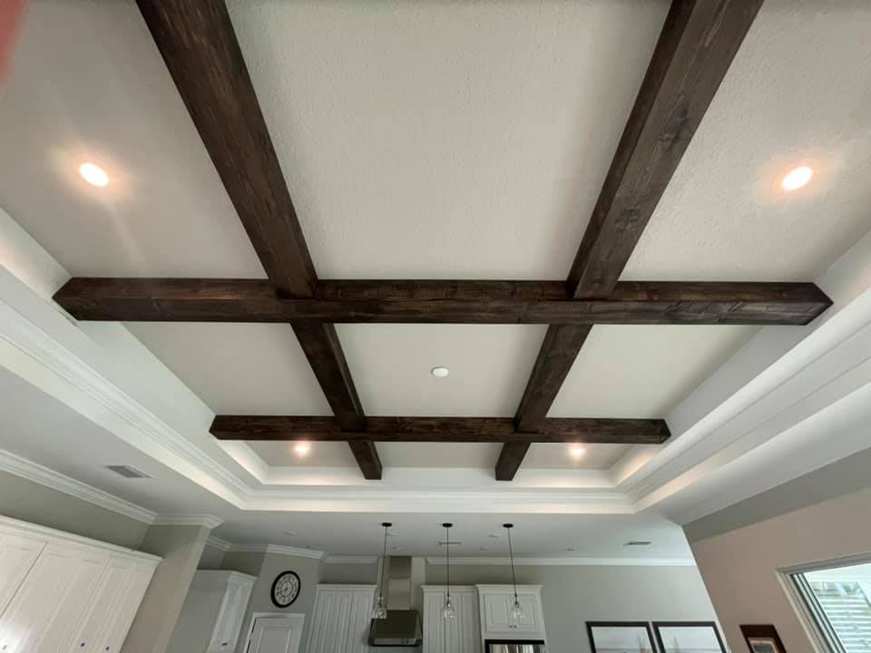 Dark wood beams crisscross a white ceiling with recessed lights in a kitchen setting.