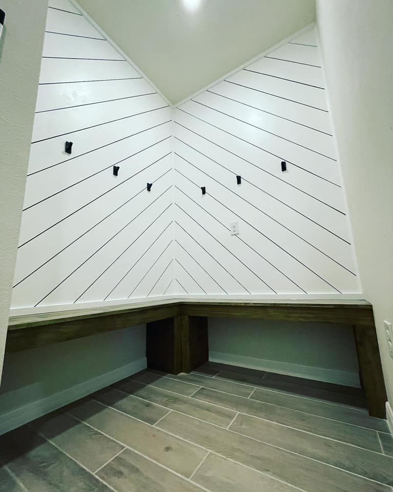 White shiplap accent wall with black trim, built-in wood bench, and tiled floor in a corner.