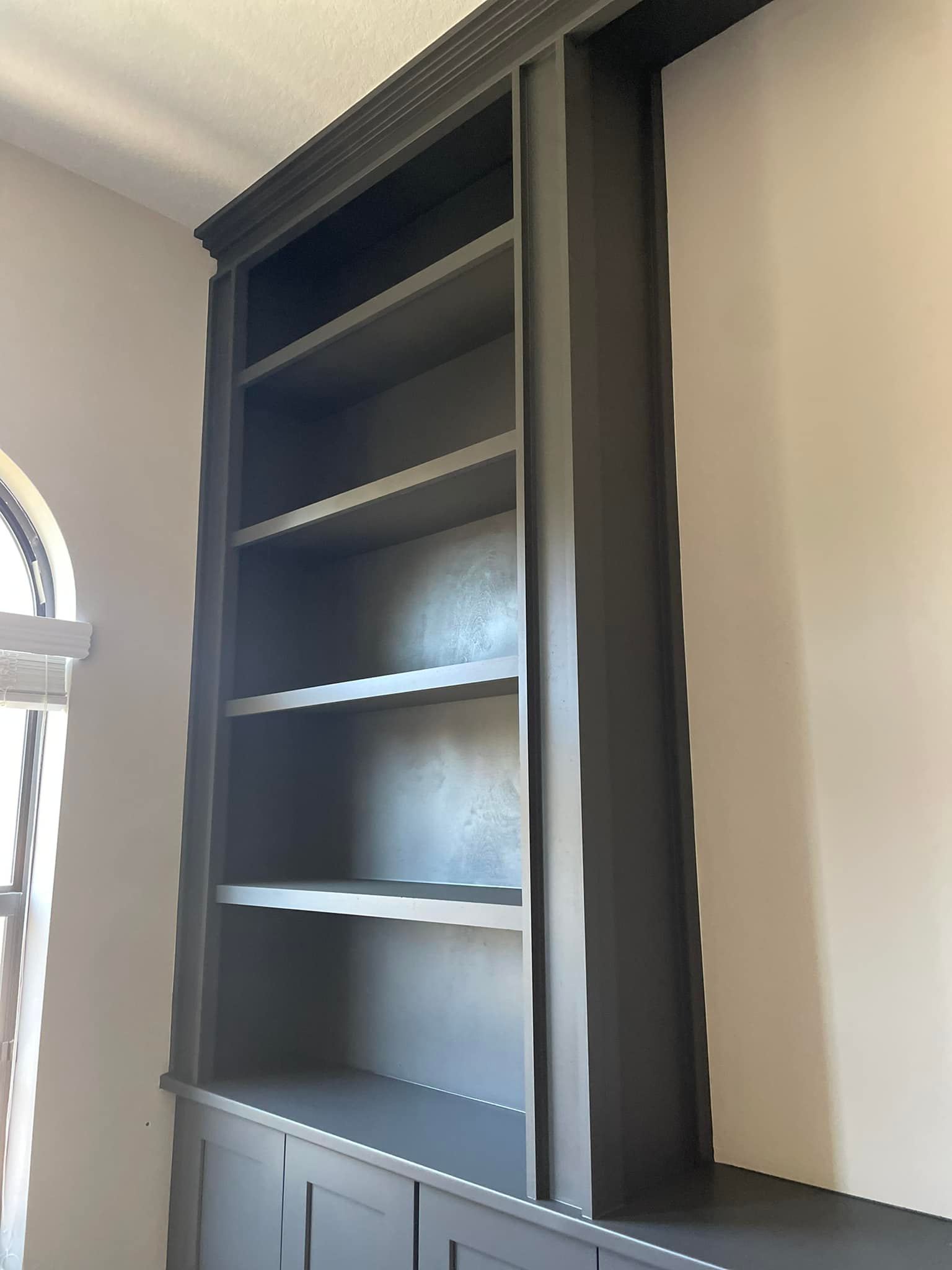 Built-in, dark gray bookshelf with four shelves, attached to a wall with light beige paint.