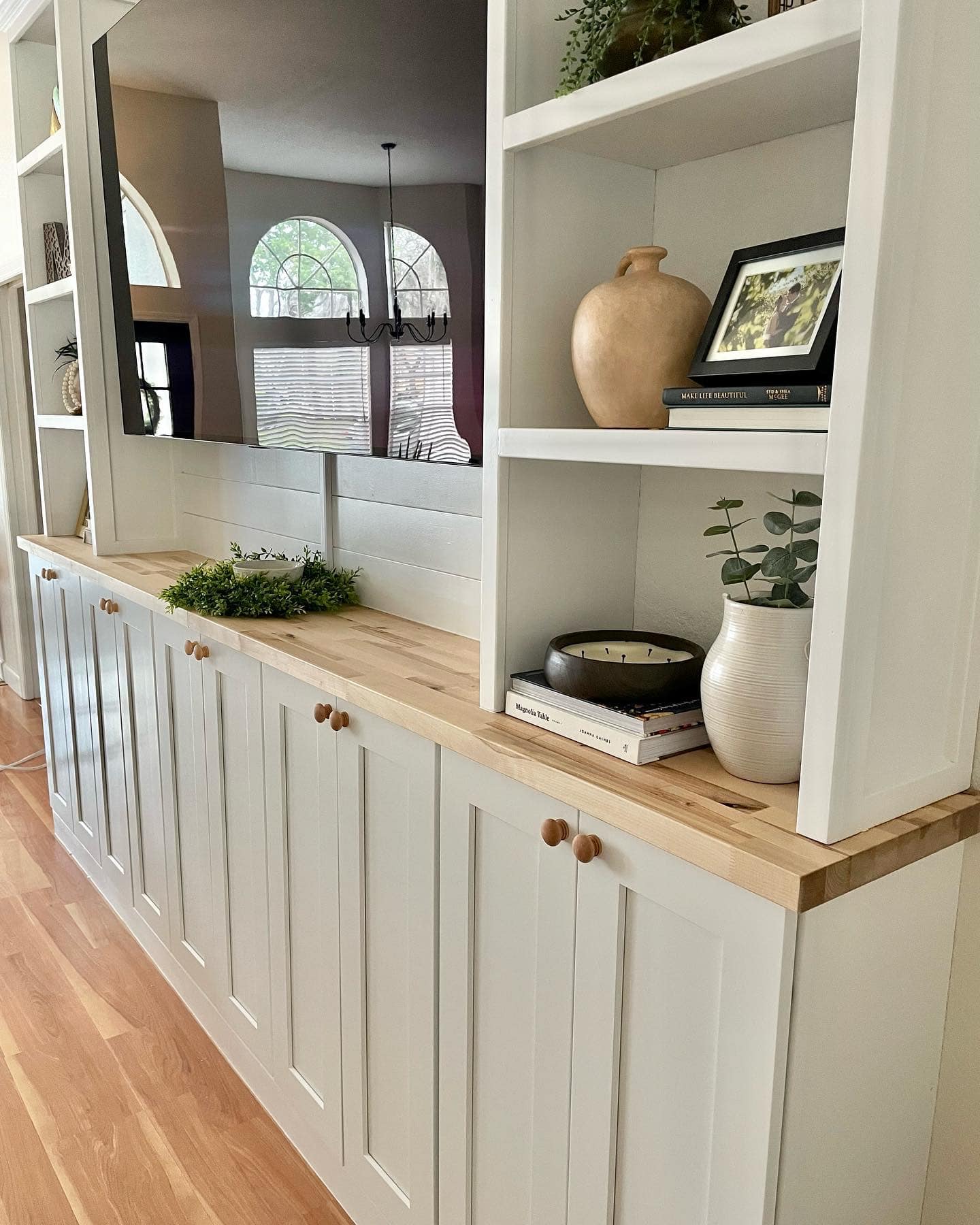 White built-in storage with wooden countertop, cabinets below, shelves above, and decorative items.