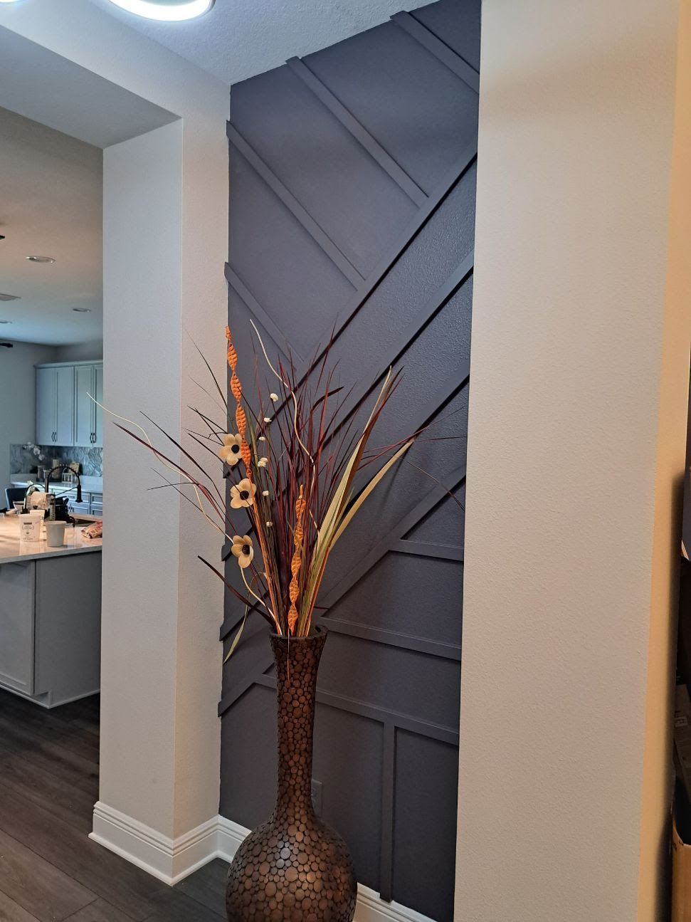 Dark gray accent wall with diagonal wood trim and a tall vase of dried flowers.