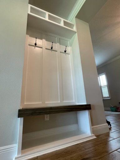 White built-in hall tree with hooks, shelf, and bench, against a light gray wall.