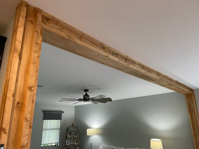 Wooden frame outlining a doorway.  Wood columns and top beam are light brown, surrounding a room with fan and lights.