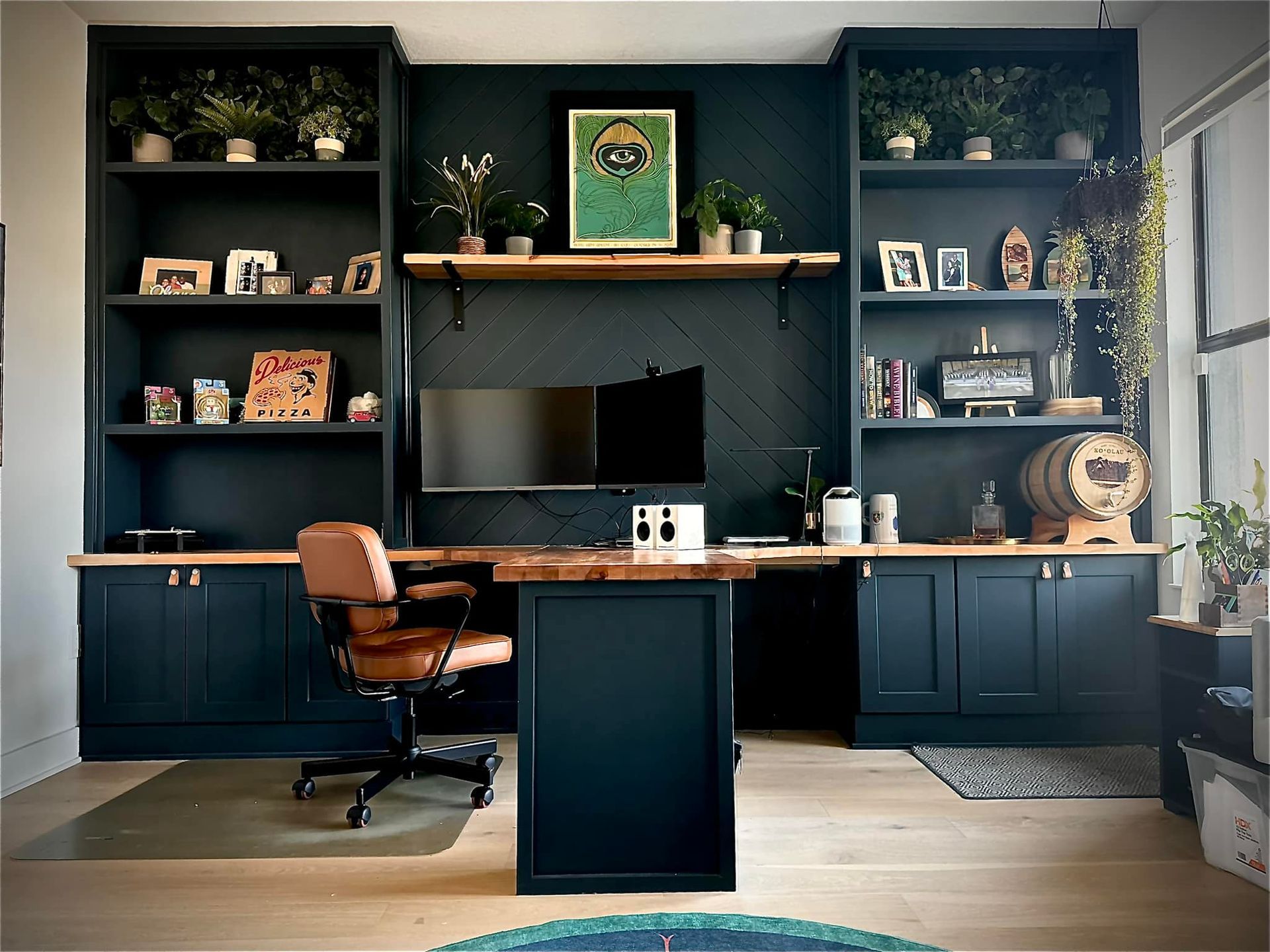 Home office with dark blue built-in shelving, wooden desk, leather chair, and various plants.