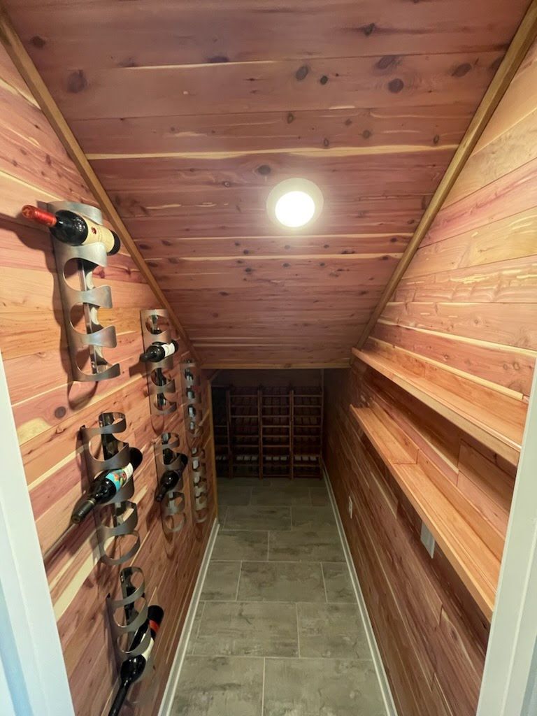 Wine cellar with cedar paneling, racks of bottles on the left, shelves on the right, and recessed lighting.