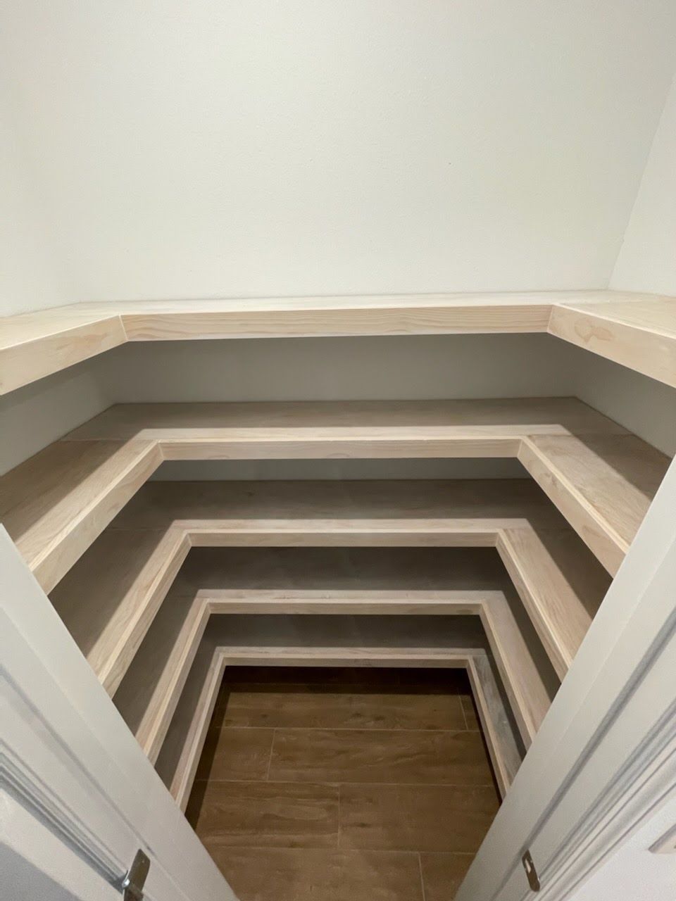 Looking down into a hexagon-shaped space with receding shelves, brown floor, and white trim.