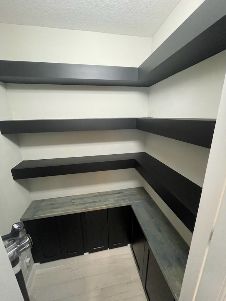 A pantry with black shelves and cabinets, gray countertop, and white walls.