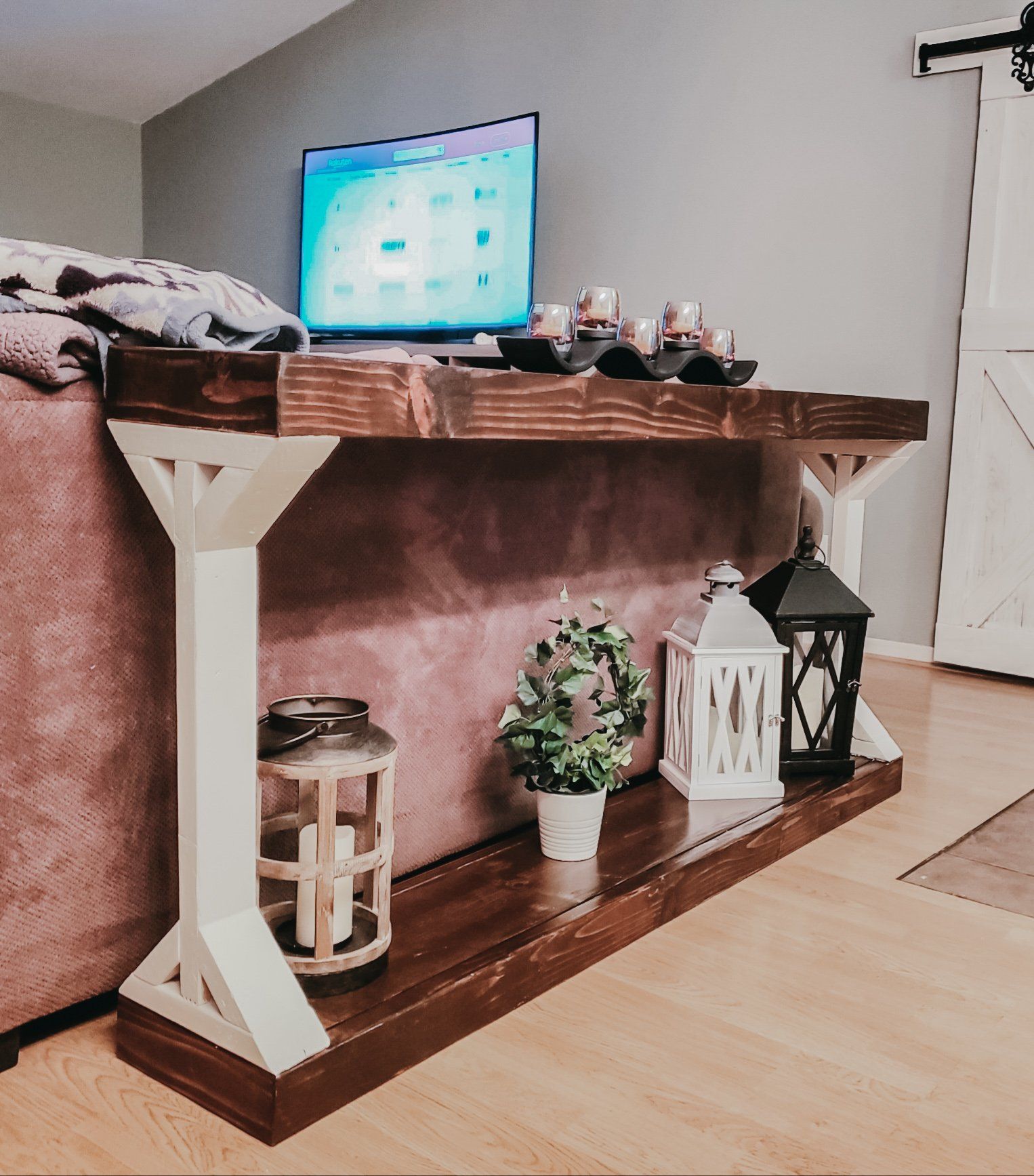 Wooden console table with a TV, decorative lanterns, and potted plant against a pink sofa.
