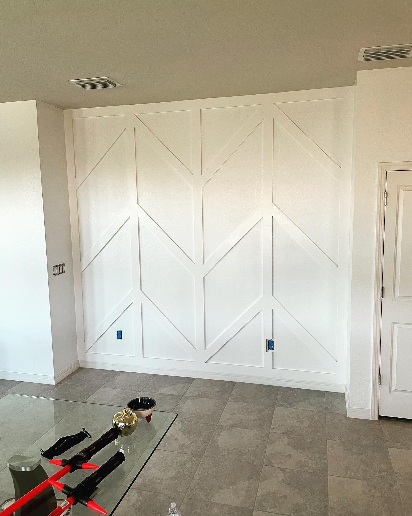 White accent wall with chevron design, unfinished, in a room with gray tiled floor.