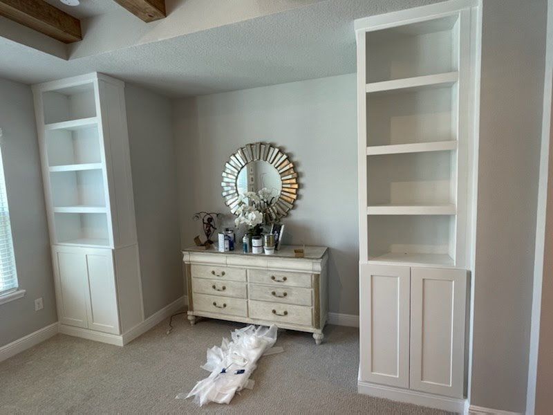 White bookshelves flank a dresser with a mirror, in a room with grey walls and carpet.