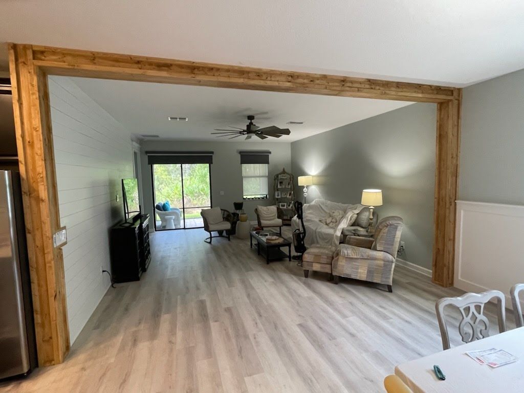 Living room with exposed wood beams. Light wood flooring, light gray walls, and comfortable furniture.