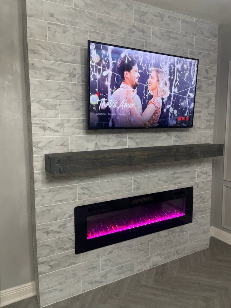Fireplace with TV mounted on gray tiled wall, black electric fireplace below, wooden shelf.