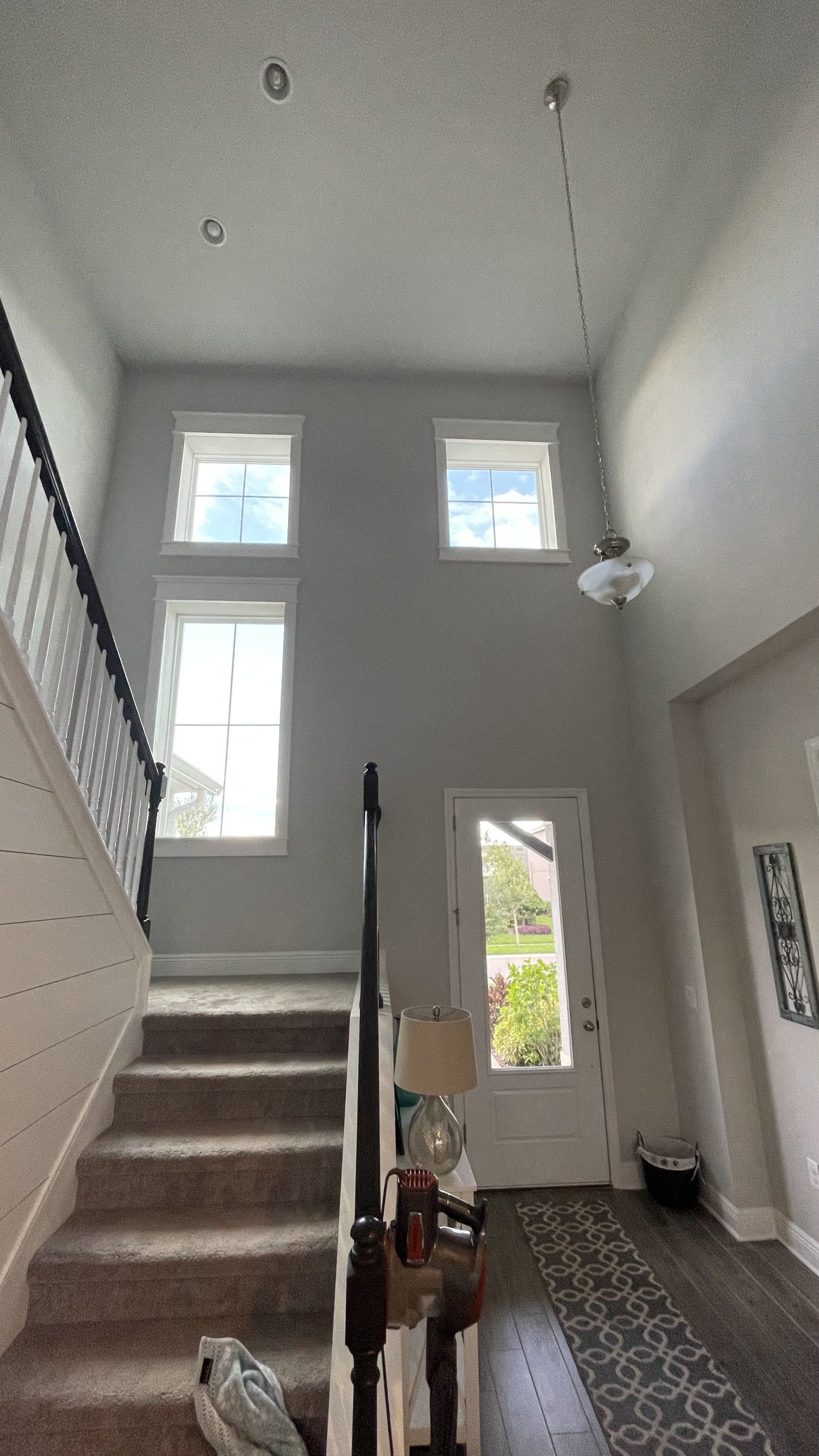 A two-story entryway with a staircase, windows, and front door. Gray walls and light fixtures.