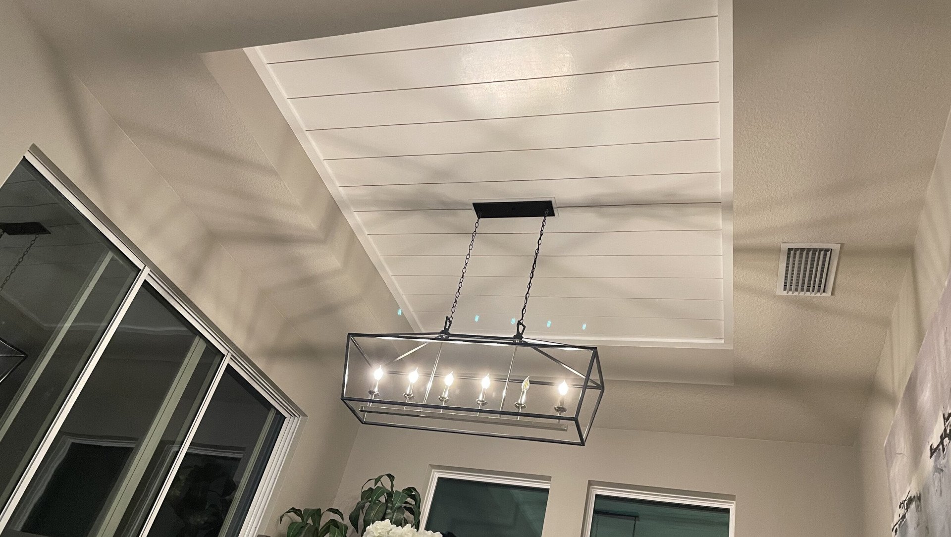 A modern chandelier hanging from a recessed white ceiling with wood-like paneling.