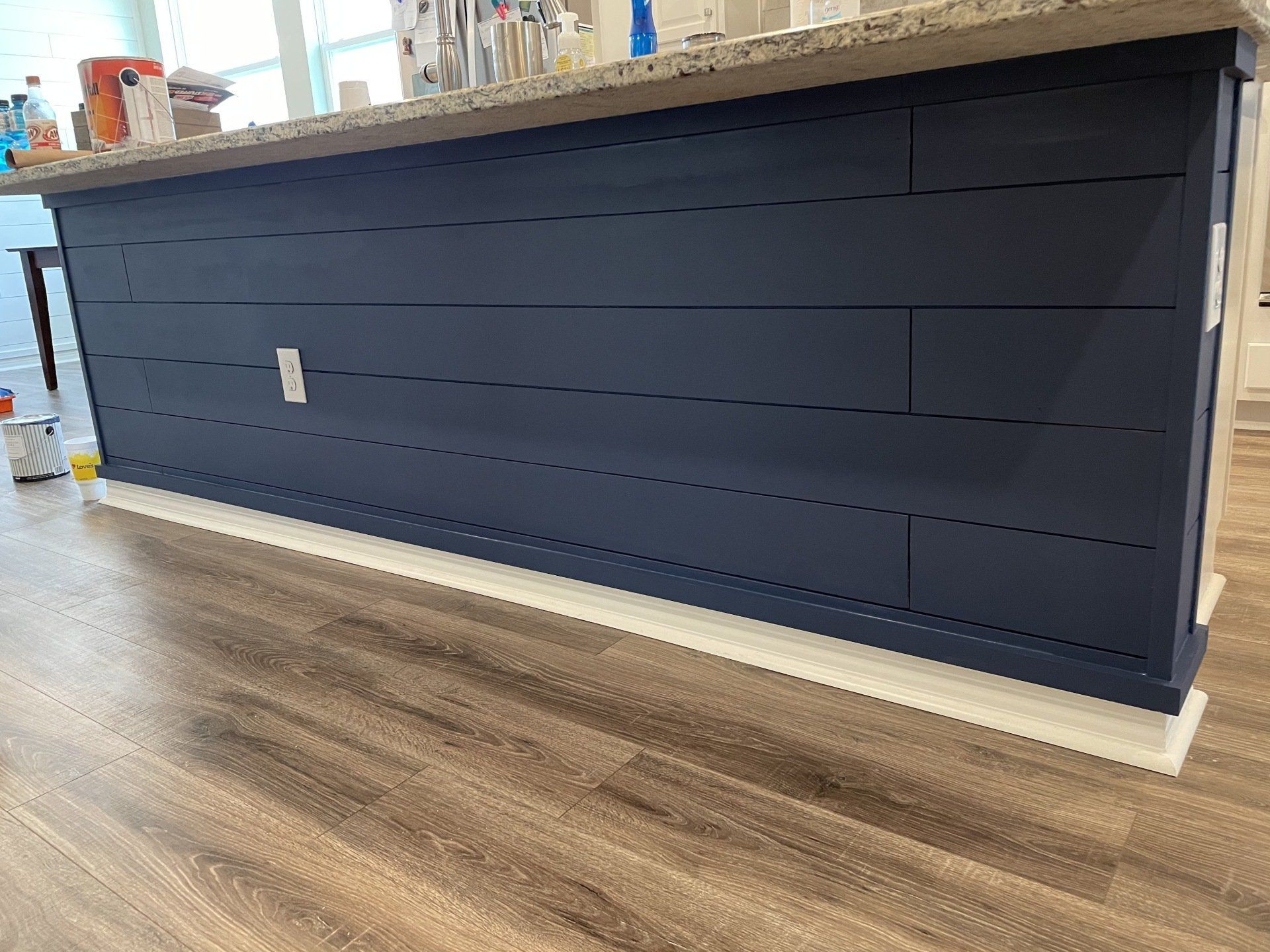 Navy blue shiplap kitchen island with a beige countertop, set on light brown wood floor.