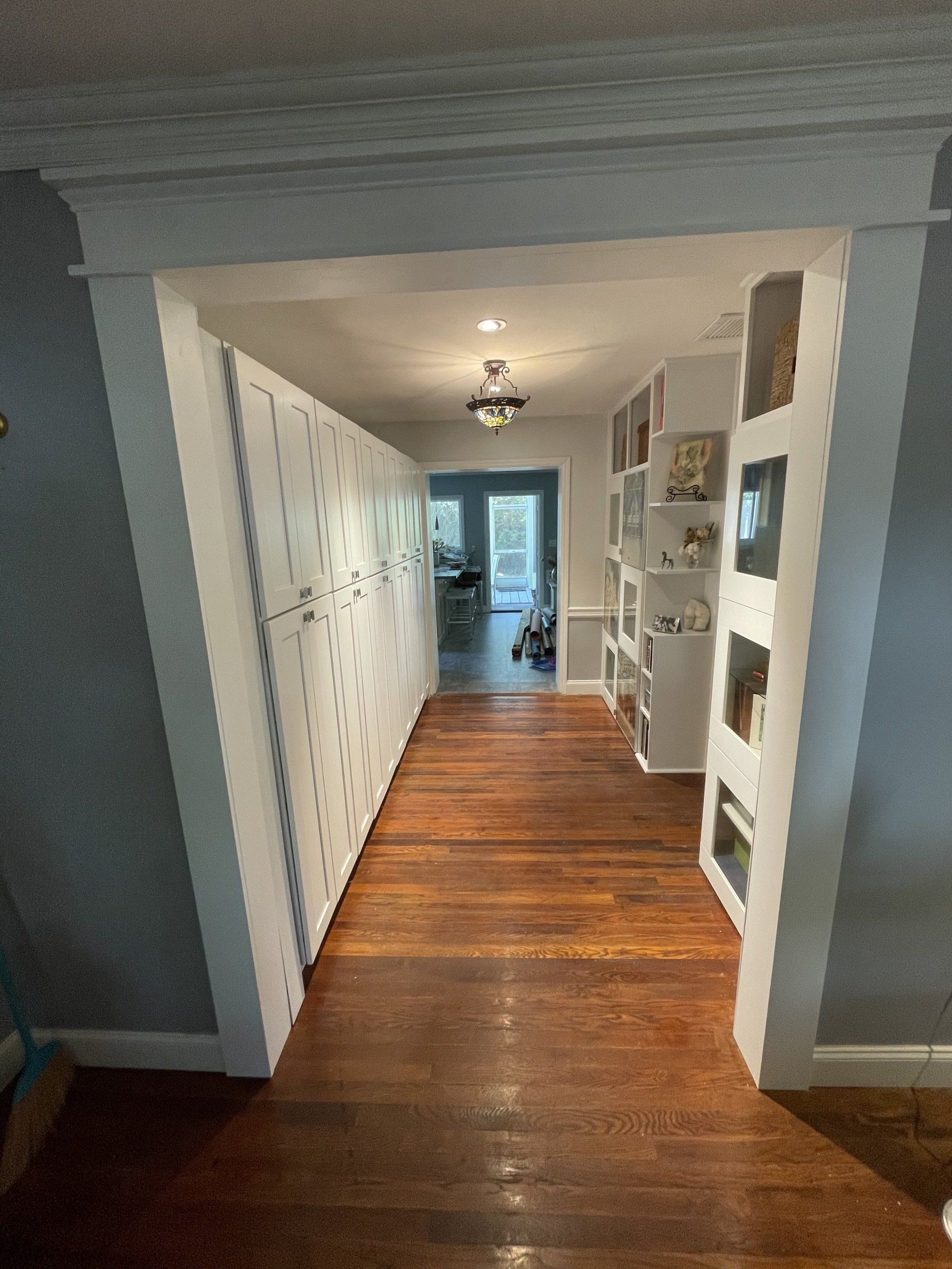 Narrow hallway with dark wood floor, built-in white cabinets on walls. Light blue walls and ceiling.
