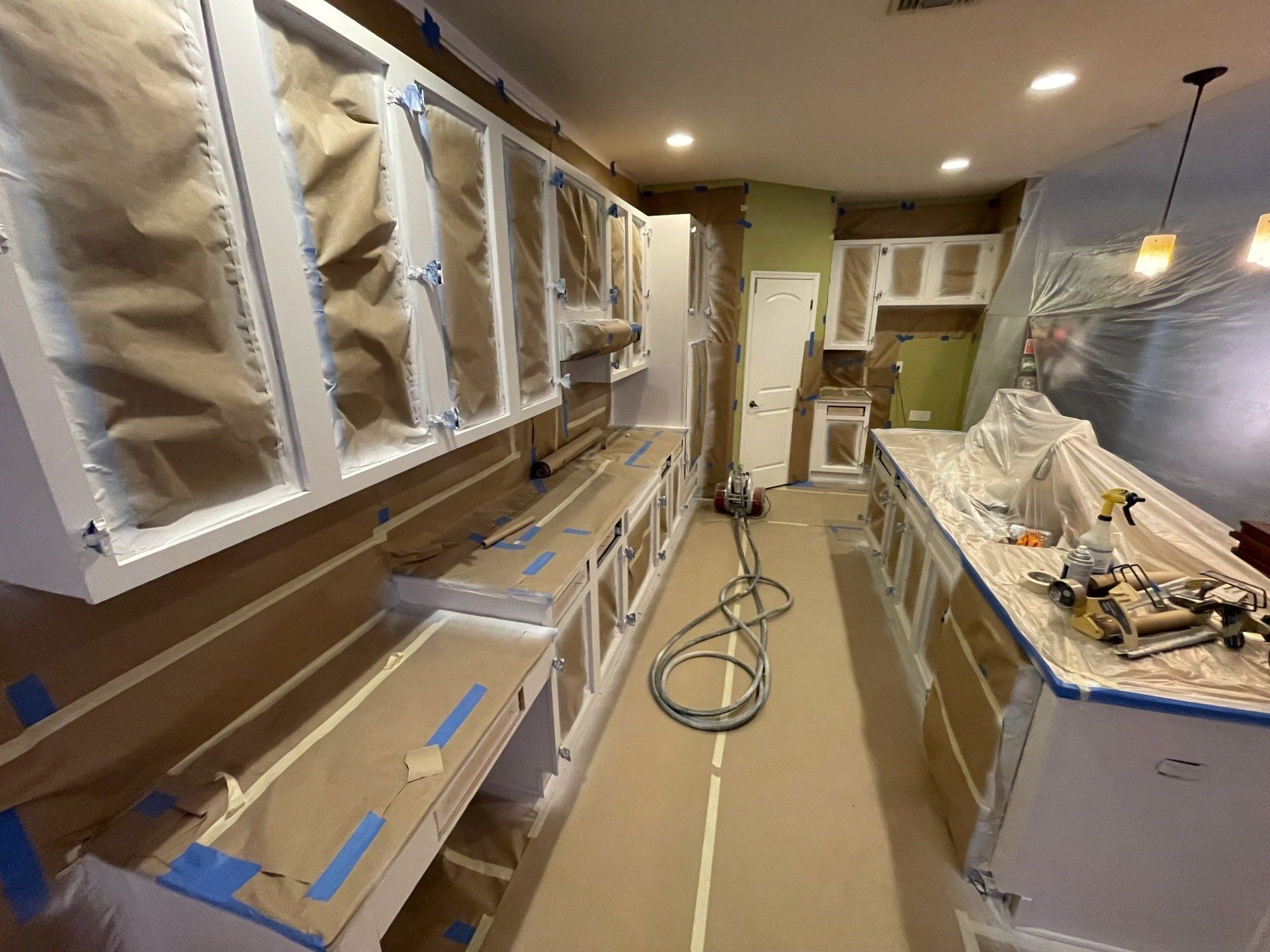 Kitchen cabinets being painted white, covered in brown paper and blue tape.
