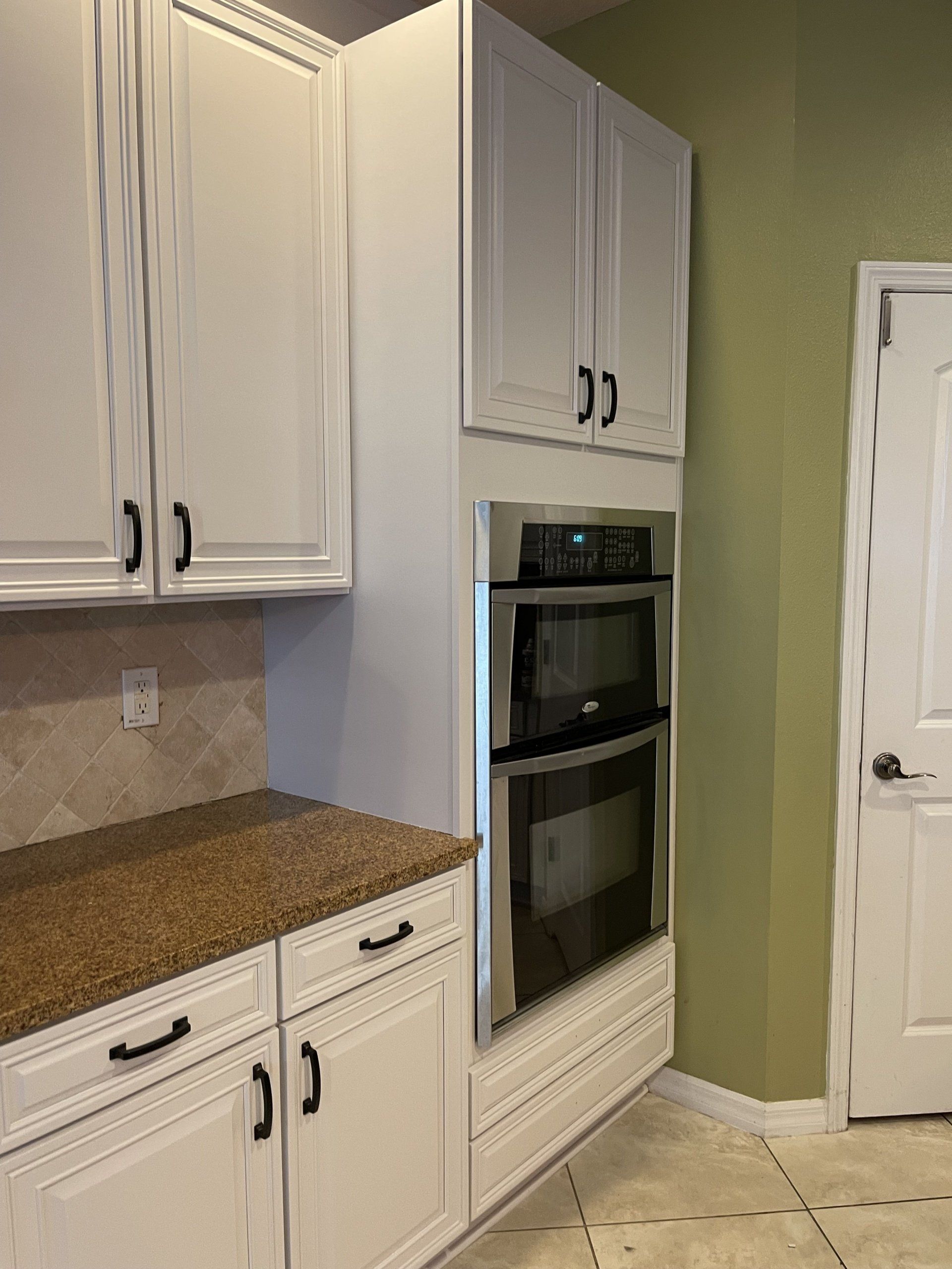 White kitchen cabinets with a built-in oven. Brown countertop and beige backsplash. Light green wall.