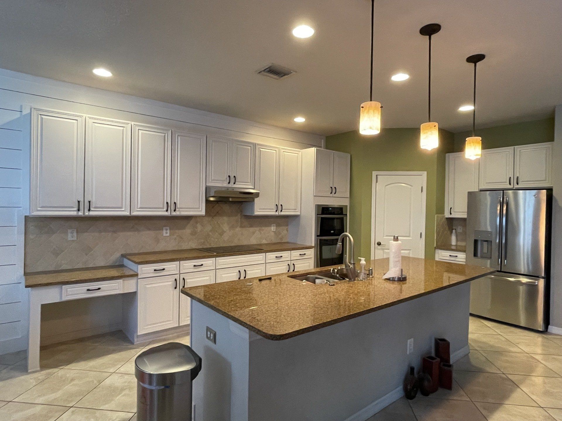 White kitchen with granite countertops, stainless steel appliances, and hanging lights.