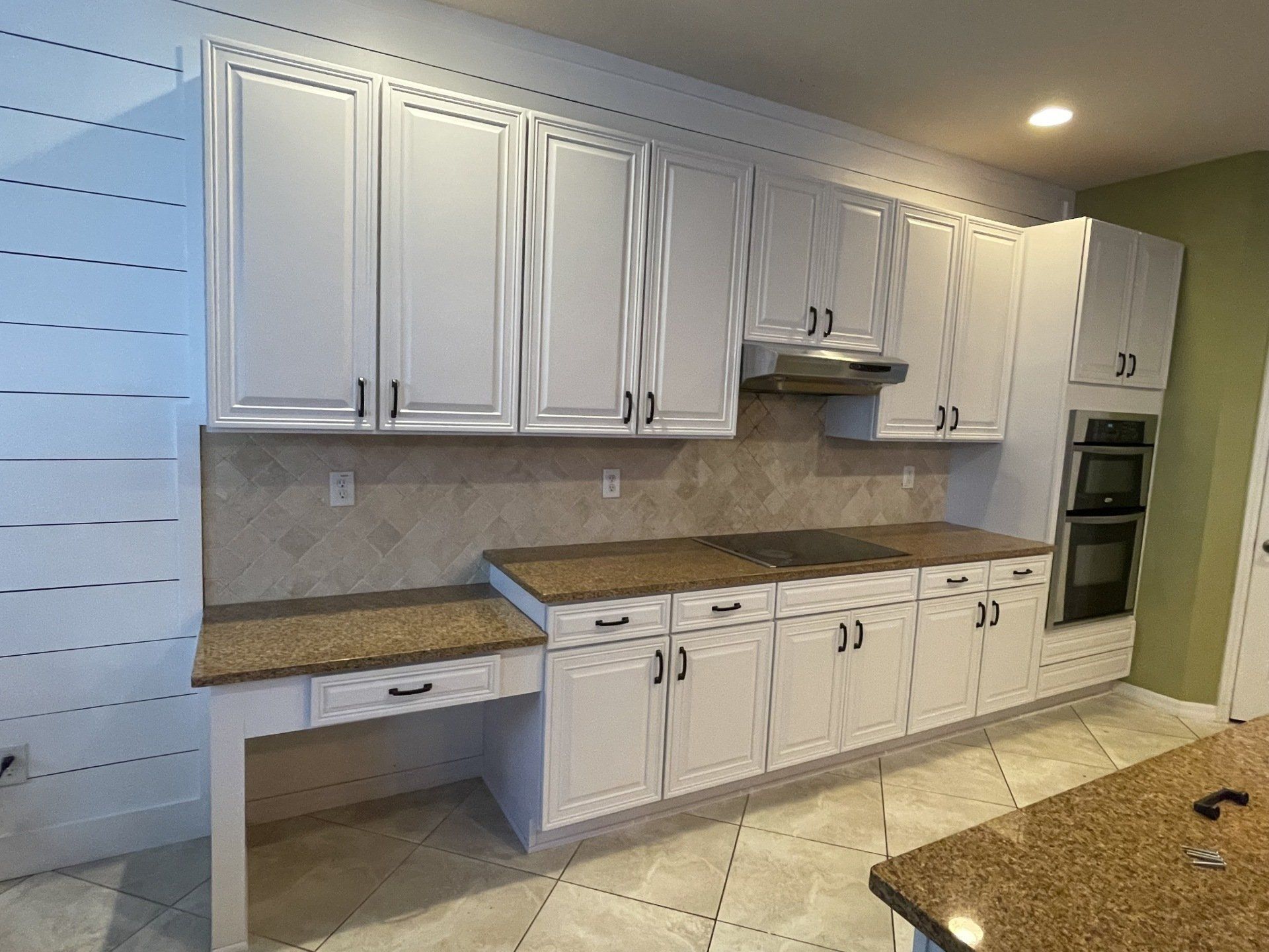 White kitchen cabinets with granite countertops and backsplash, oven, range hood.