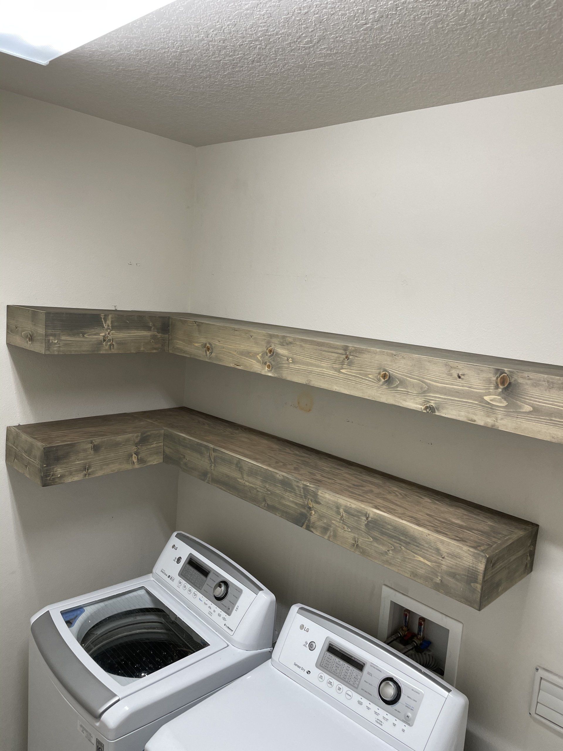 Laundy room with white appliances, weathered wooden shelves above.