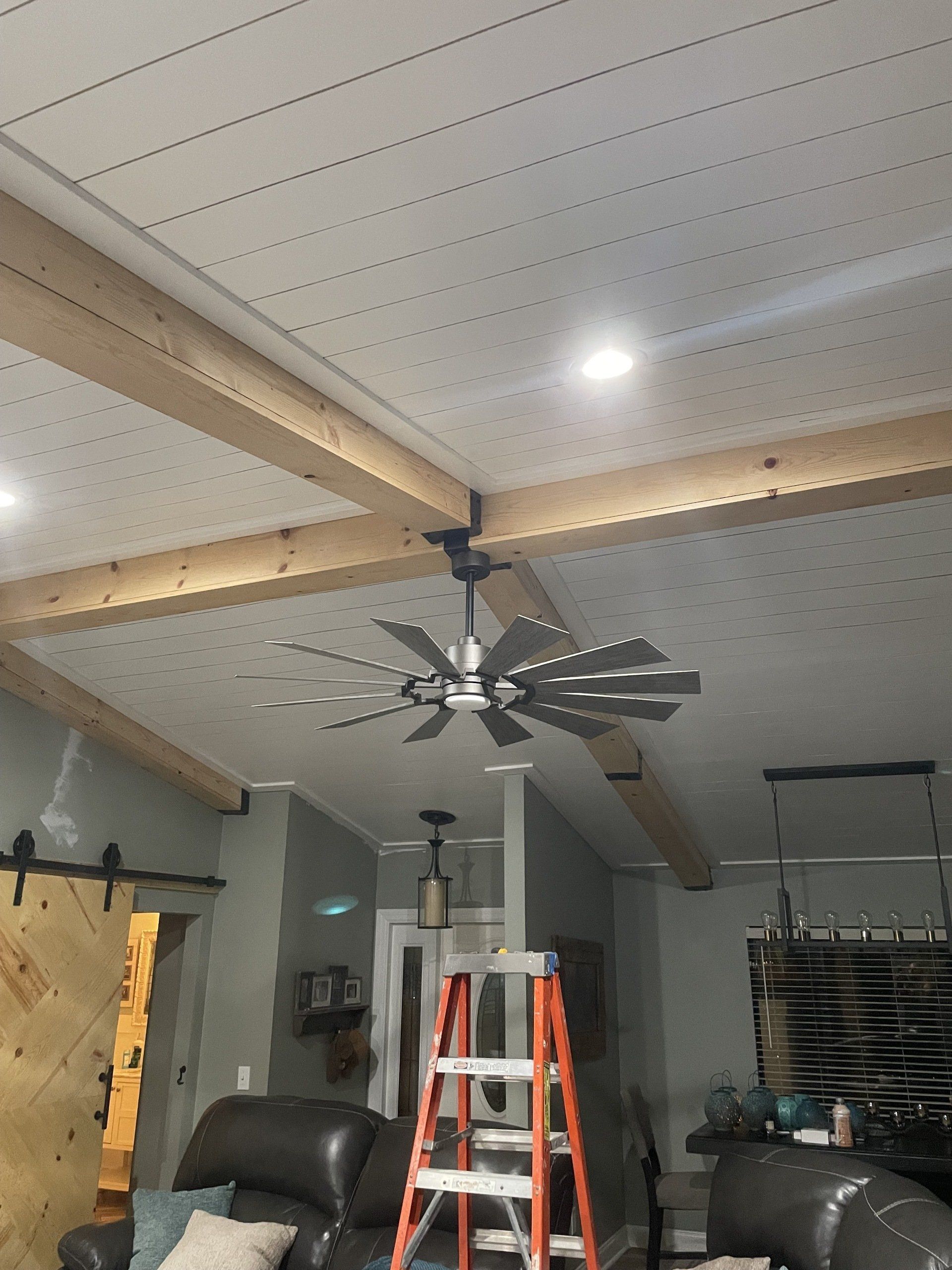 Ceiling fan with decorative beams and recessed lights in a living room. A ladder stands near the fan.