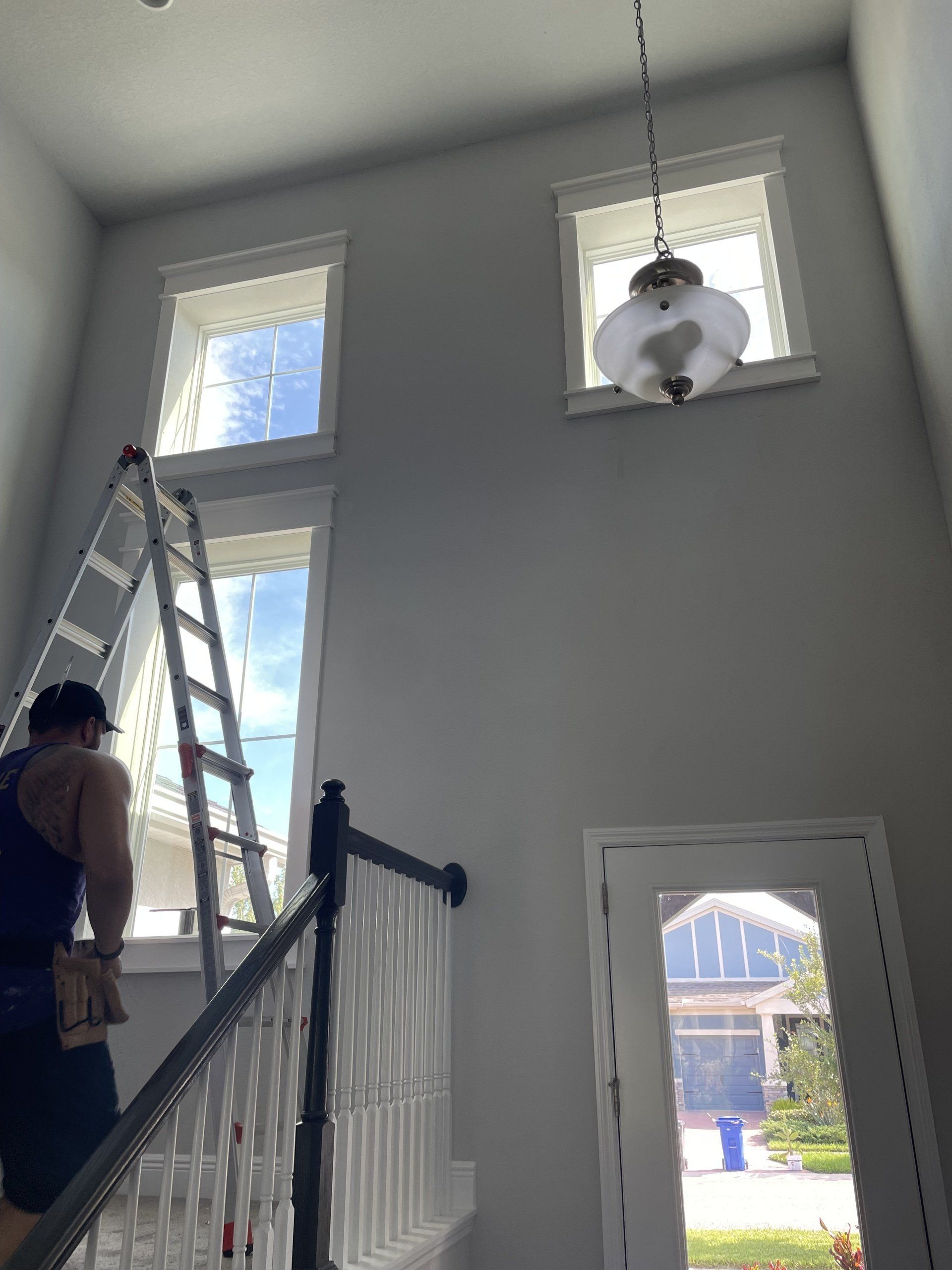 Person on ladder cleaning high windows in a two-story foyer with a chandelier.