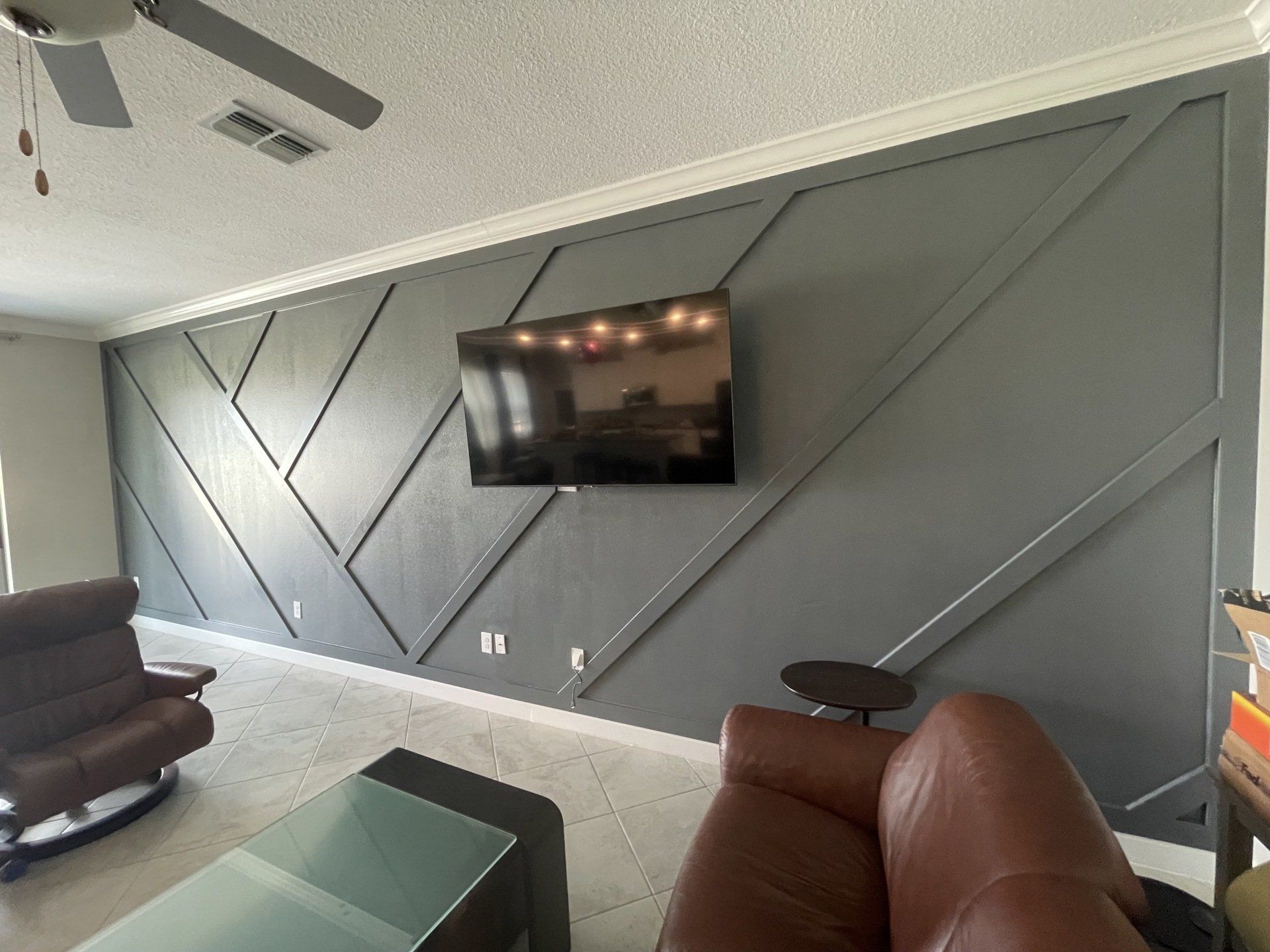 Living room with grey geometric accent wall, TV, and leather furniture.
