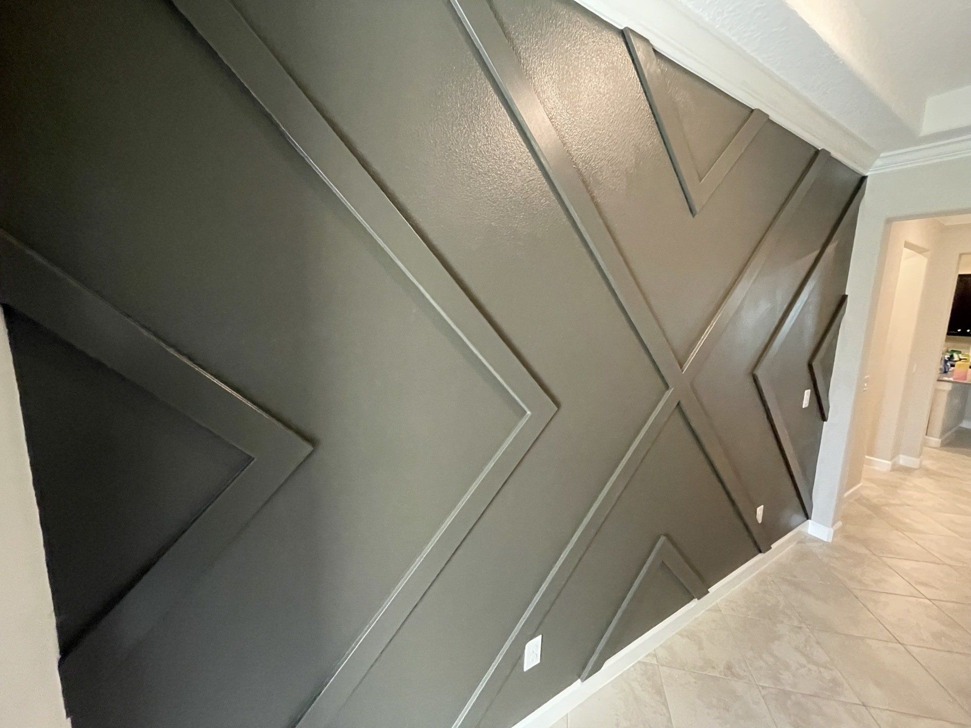Gray geometric accent wall with white trim and an adjacent hallway.