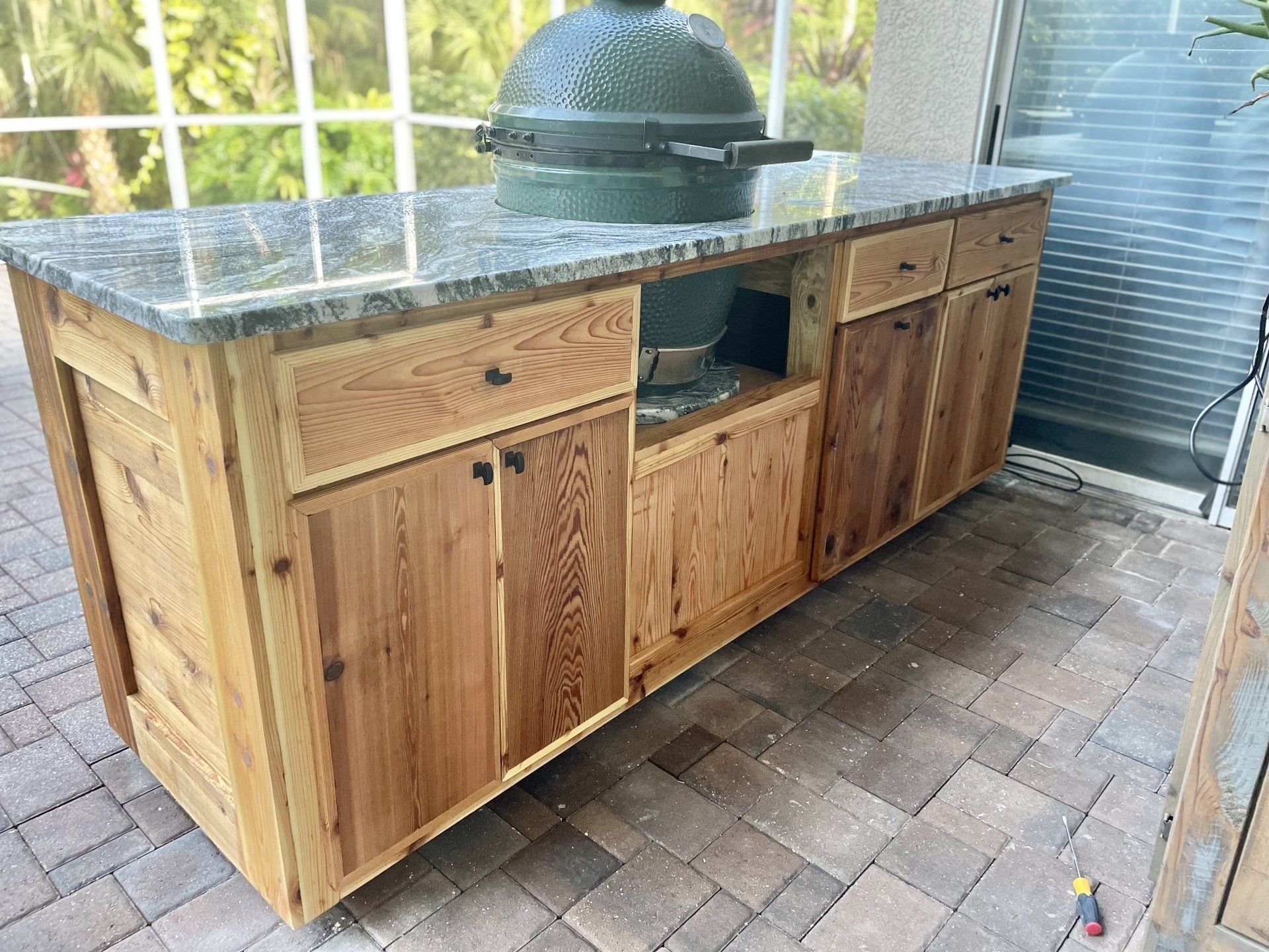 Outdoor kitchen island with granite countertop and a green egg grill.